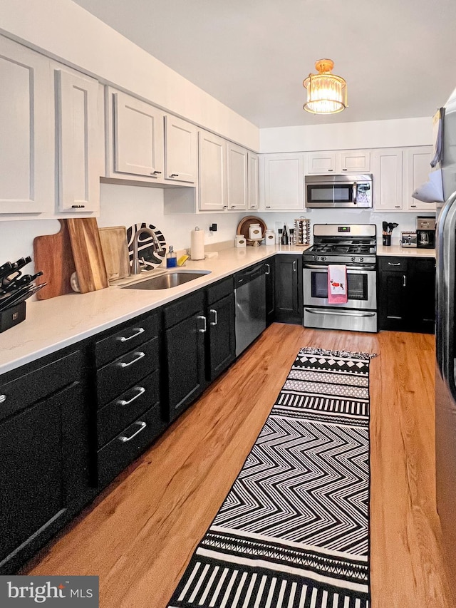 kitchen featuring light wood-type flooring, sink, stainless steel appliances, and white cabinetry