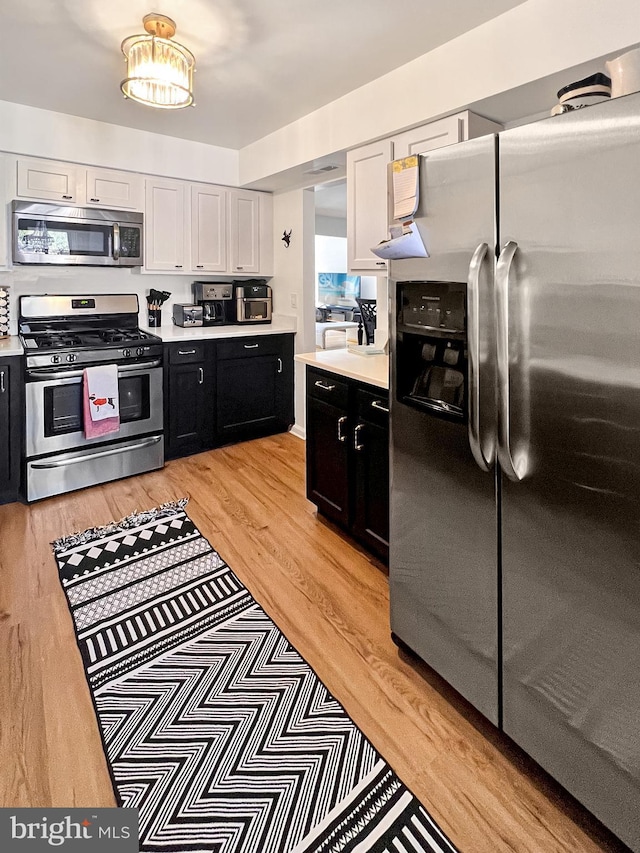 kitchen with appliances with stainless steel finishes, light hardwood / wood-style flooring, and white cabinetry