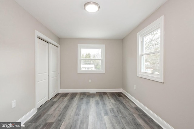 unfurnished bedroom with dark hardwood / wood-style floors, multiple windows, and a closet