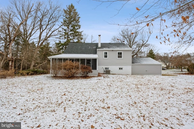 snow covered back of property featuring central air condition unit and a sunroom