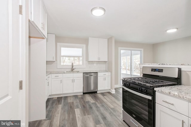 kitchen with light stone countertops, stainless steel appliances, white cabinetry, and sink