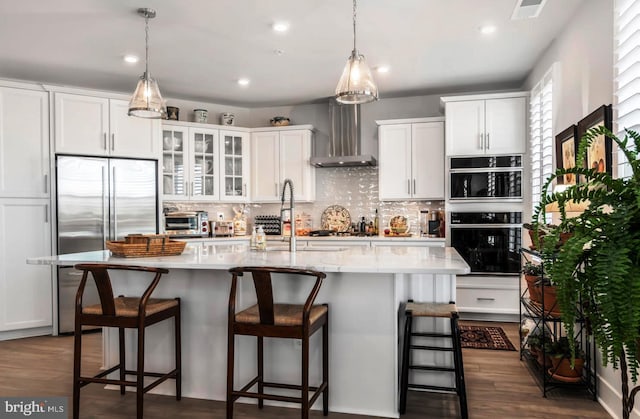 kitchen with white cabinets, a kitchen island with sink, and wall chimney exhaust hood