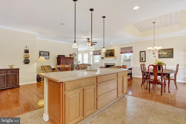 kitchen featuring a center island, light brown cabinets, hanging light fixtures, a tray ceiling, and ceiling fan with notable chandelier