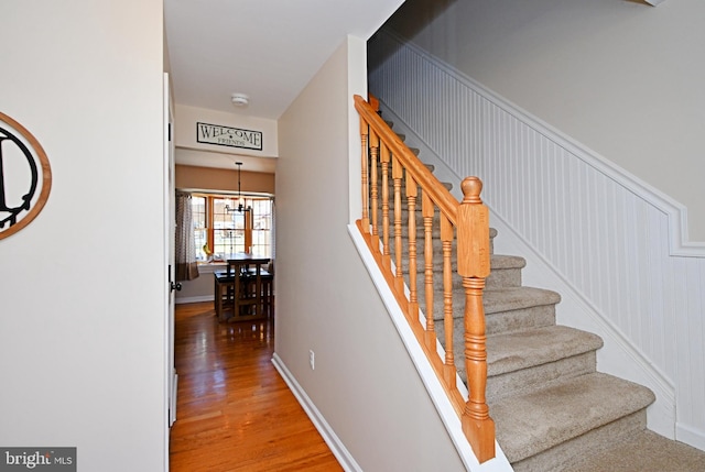 stairs featuring hardwood / wood-style floors and an inviting chandelier