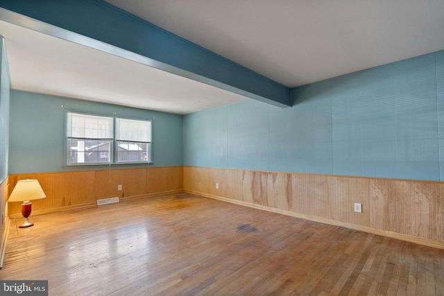 unfurnished room featuring wooden walls, beamed ceiling, and light wood-type flooring