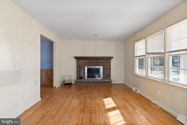 unfurnished living room featuring a brick fireplace and light hardwood / wood-style flooring