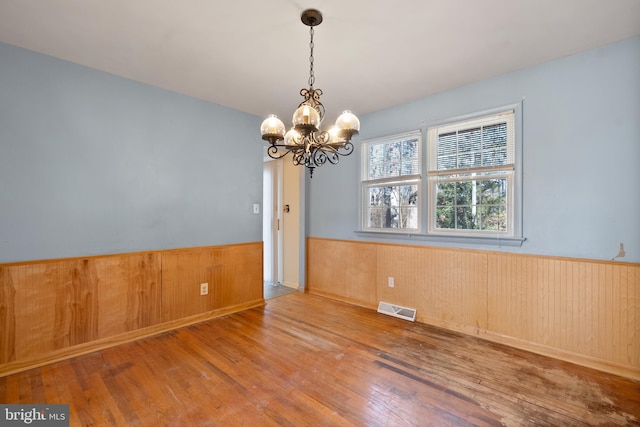 unfurnished room with wood-type flooring, wood walls, and a chandelier