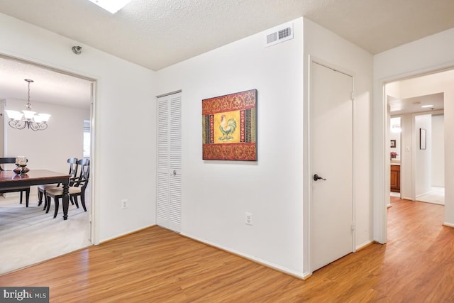 hall with wood-type flooring, a notable chandelier, and a textured ceiling