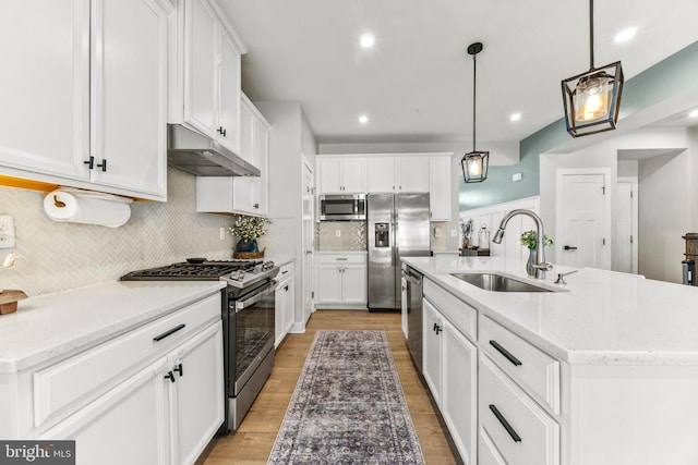 kitchen featuring a kitchen island with sink, stainless steel appliances, hanging light fixtures, sink, and white cabinetry