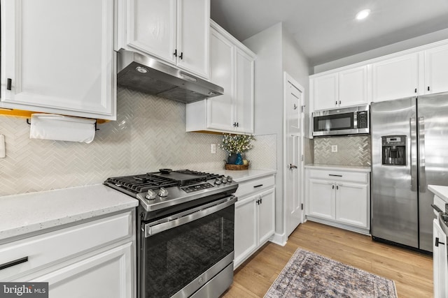 kitchen with stainless steel appliances, white cabinets, light stone counters, light wood-type flooring, and tasteful backsplash