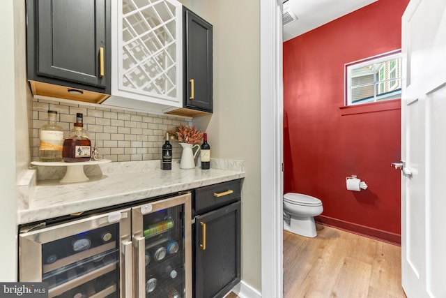 kitchen with light stone counters, decorative backsplash, light wood-type flooring, and wine cooler