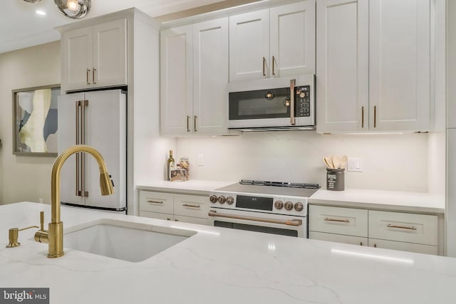 kitchen with light stone counters, high end appliances, backsplash, white cabinets, and sink