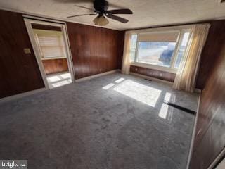 unfurnished bedroom with carpet flooring, wooden walls, and ceiling fan