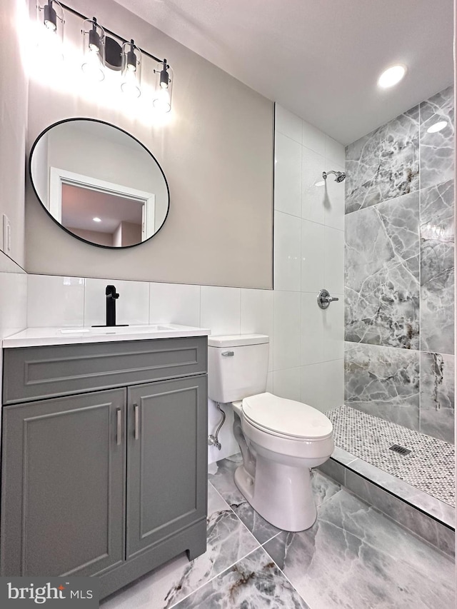 bathroom featuring vanity, toilet, tile walls, and a tile shower