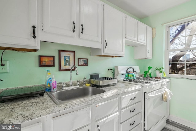 kitchen with a sink, baseboards, white cabinetry, and gas range gas stove