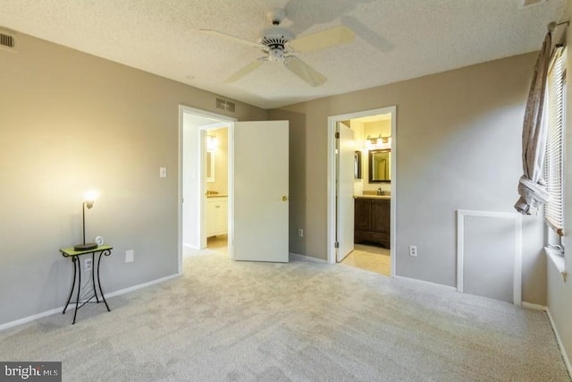 unfurnished bedroom featuring ceiling fan, light colored carpet, connected bathroom, and a textured ceiling