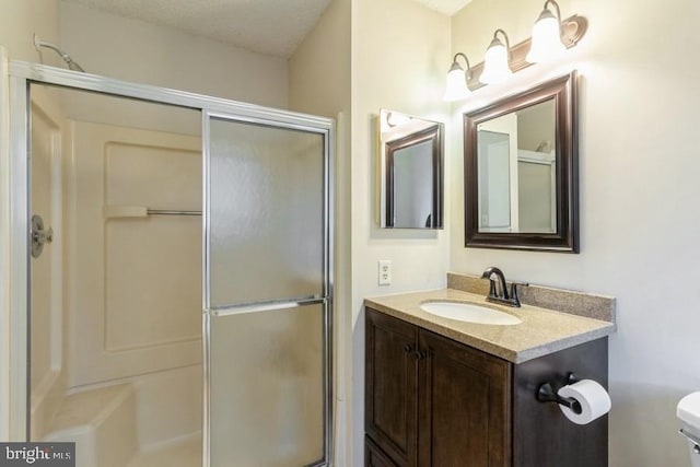 bathroom with a textured ceiling, vanity, a shower with shower door, and toilet