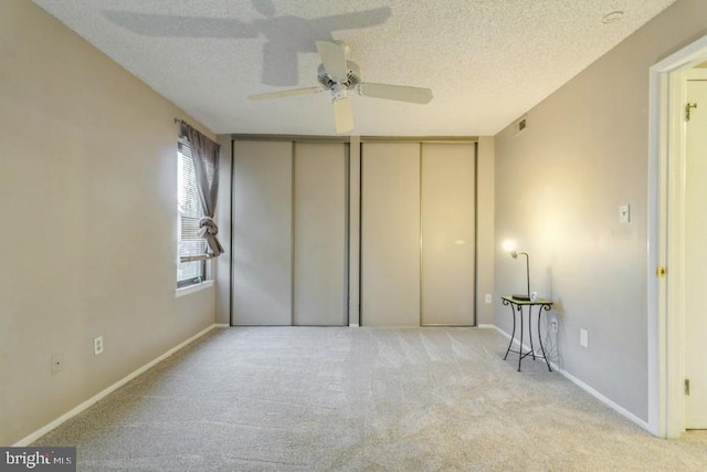 unfurnished bedroom featuring multiple closets, ceiling fan, a textured ceiling, and light colored carpet