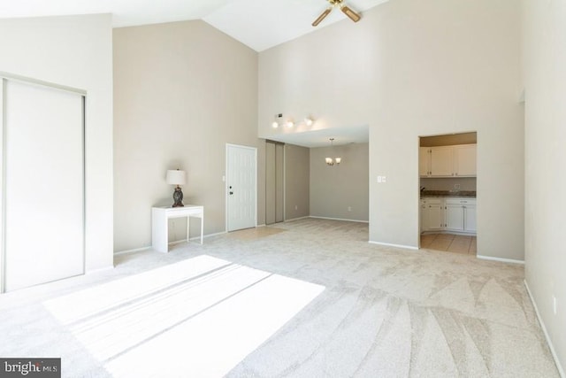 interior space with ceiling fan with notable chandelier, high vaulted ceiling, and light carpet