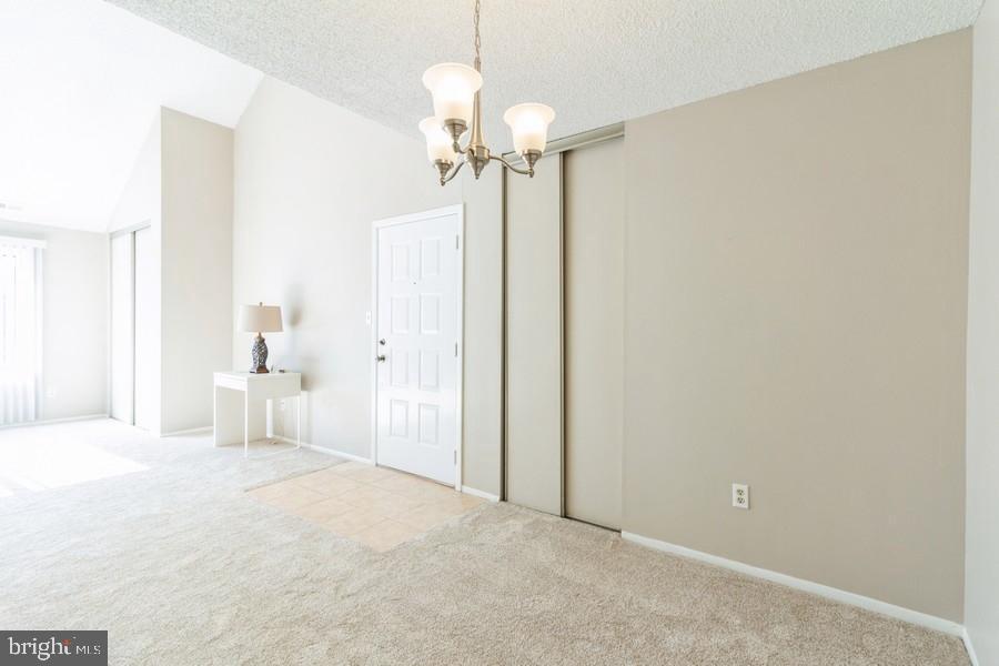 carpeted spare room featuring lofted ceiling, a textured ceiling, and a notable chandelier