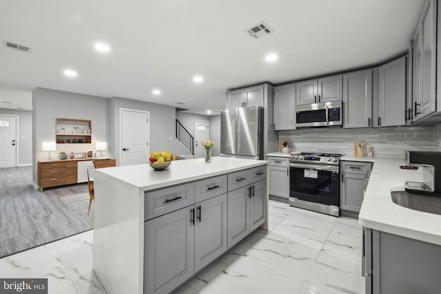 kitchen with a center island, sink, decorative backsplash, gray cabinets, and stainless steel appliances