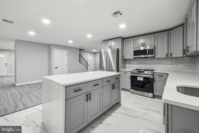 kitchen featuring decorative backsplash, appliances with stainless steel finishes, a center island, and gray cabinets