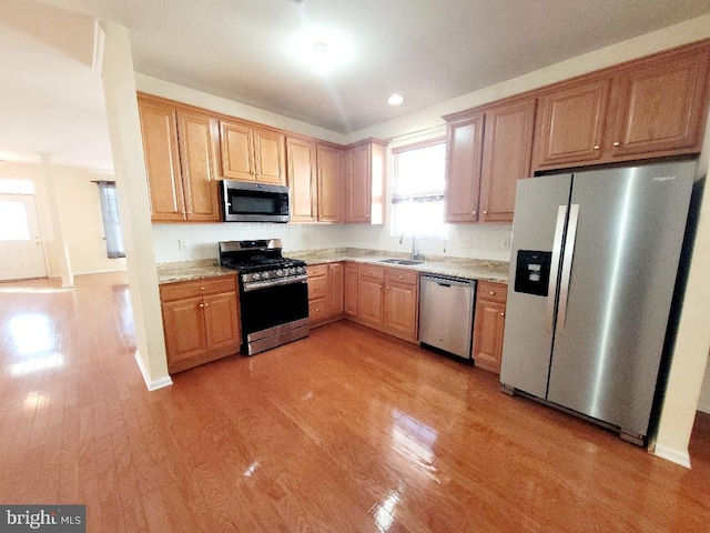 kitchen featuring appliances with stainless steel finishes, light wood-type flooring, light stone counters, and sink