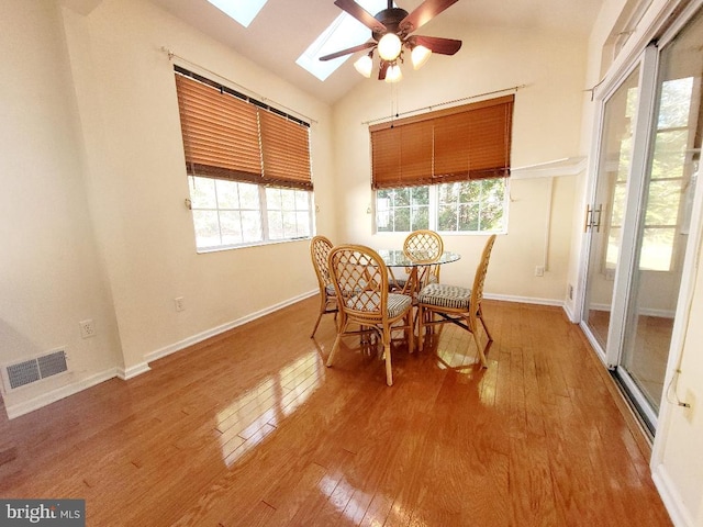 dining area with ceiling fan, vaulted ceiling with skylight, and wood-type flooring