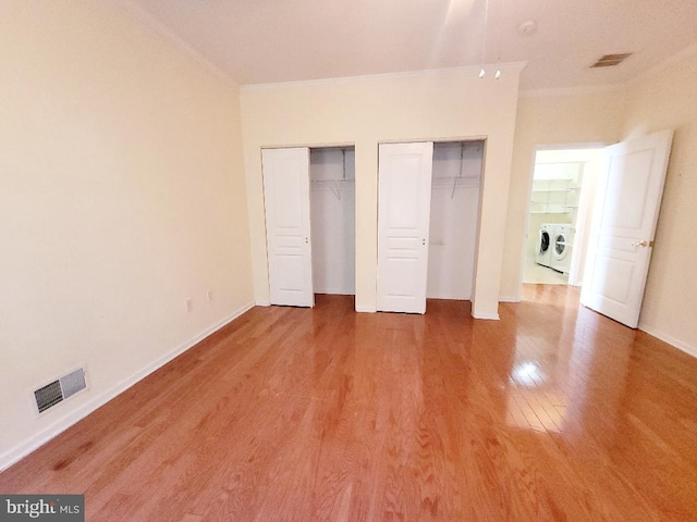 unfurnished bedroom featuring two closets, washing machine and dryer, crown molding, and wood-type flooring