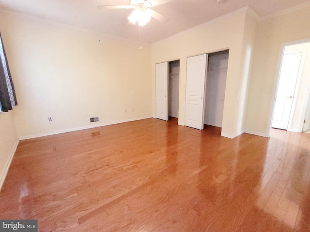 unfurnished bedroom featuring wood-type flooring, multiple closets, ceiling fan, and crown molding