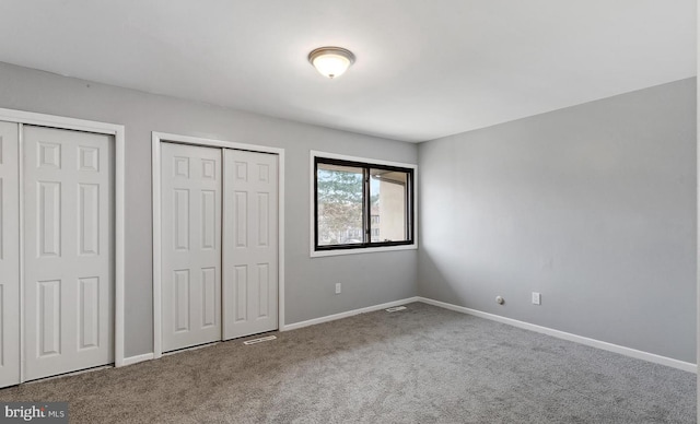 unfurnished bedroom featuring carpet floors and two closets