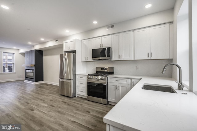 kitchen with backsplash, wood-type flooring, sink, white cabinetry, and stainless steel appliances