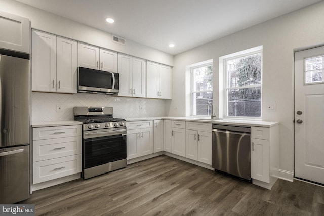 kitchen with white cabinetry, stainless steel appliances, dark hardwood / wood-style floors, tasteful backsplash, and sink