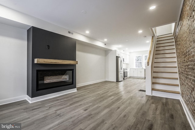 unfurnished living room with visible vents, a glass covered fireplace, wood finished floors, stairs, and recessed lighting