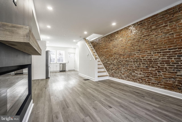 unfurnished living room featuring wood-type flooring and brick wall