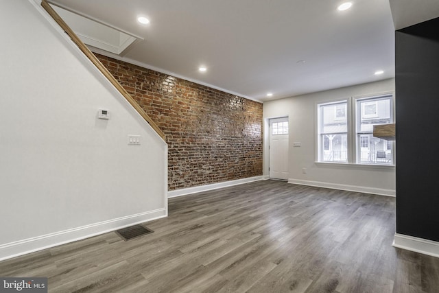 unfurnished living room featuring brick wall and hardwood / wood-style floors