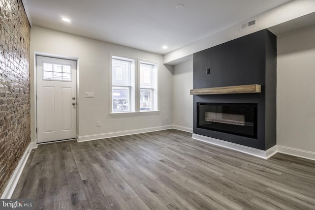 unfurnished living room featuring a large fireplace, dark wood-type flooring, and a wealth of natural light