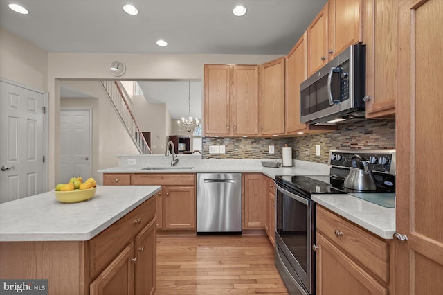 kitchen with decorative light fixtures, sink, kitchen peninsula, stainless steel appliances, and light hardwood / wood-style flooring