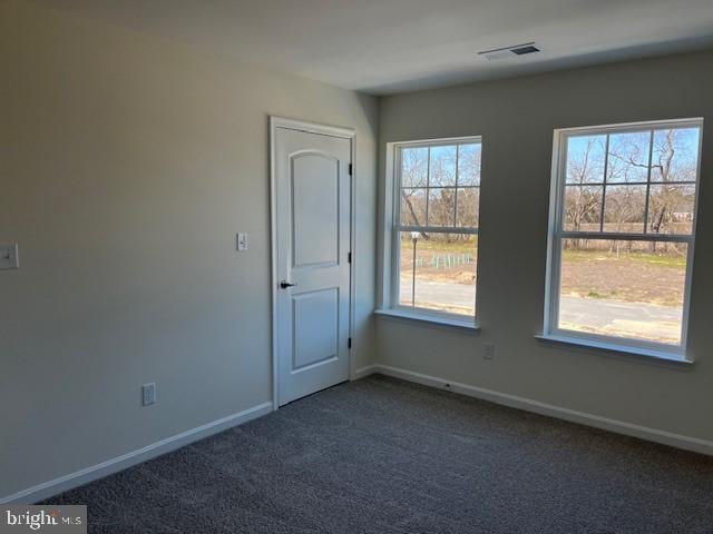 empty room with dark carpet, visible vents, and baseboards