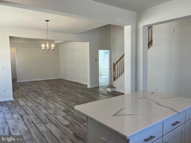 interior space with an inviting chandelier, light stone countertops, wood finished floors, decorative light fixtures, and baseboards