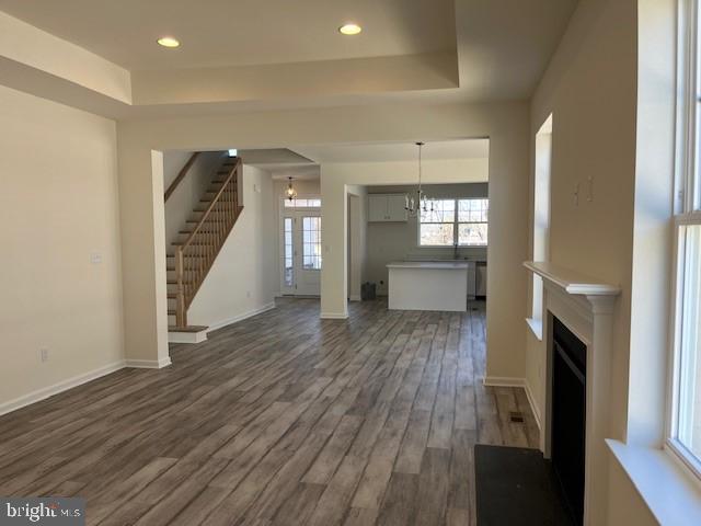 unfurnished living room with a raised ceiling, a chandelier, a fireplace, stairs, and dark wood-type flooring