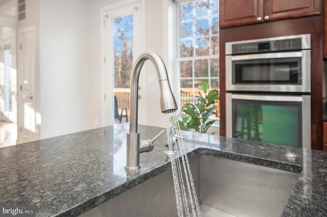 kitchen with double oven, sink, and dark stone counters