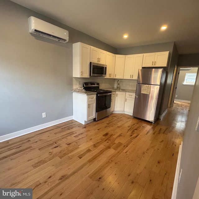 kitchen with a wall mounted air conditioner, sink, light stone countertops, appliances with stainless steel finishes, and white cabinetry