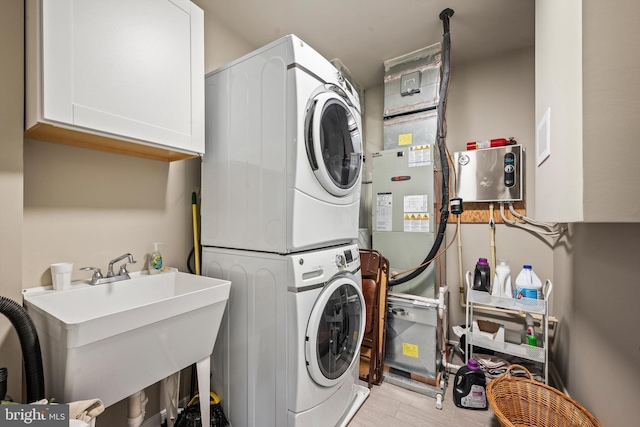 laundry room with sink, stacked washing maching and dryer, light hardwood / wood-style floors, and cabinets