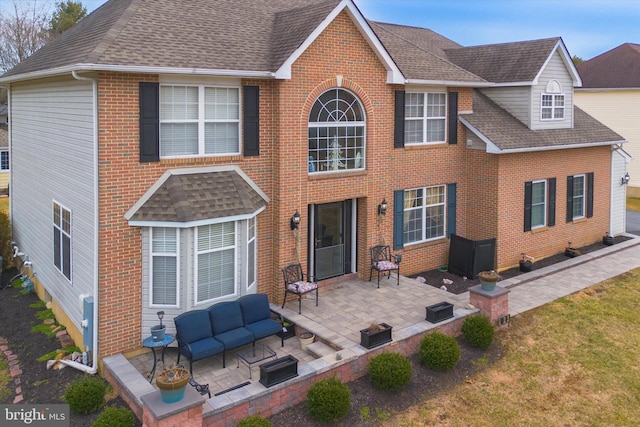 view of front facade featuring an outdoor hangout area, a shingled roof, a patio area, and brick siding