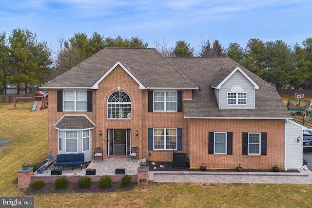 view of front of property with a shingled roof, a patio, a front lawn, a playground, and brick siding