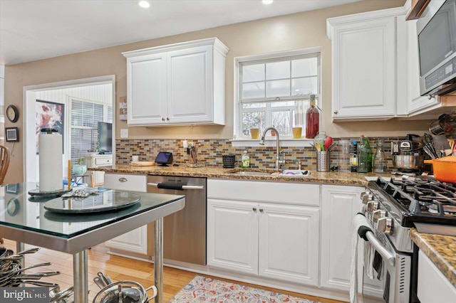 kitchen with appliances with stainless steel finishes, a sink, white cabinetry, and decorative backsplash