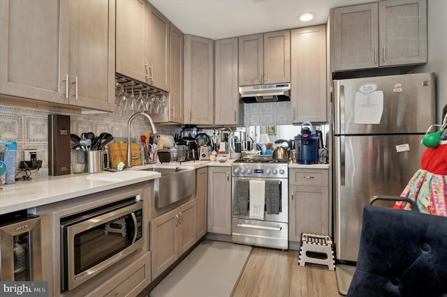 kitchen with under cabinet range hood, appliances with stainless steel finishes, light countertops, and a sink