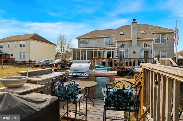 deck featuring an outdoor kitchen, area for grilling, a sunroom, fence, and a sink