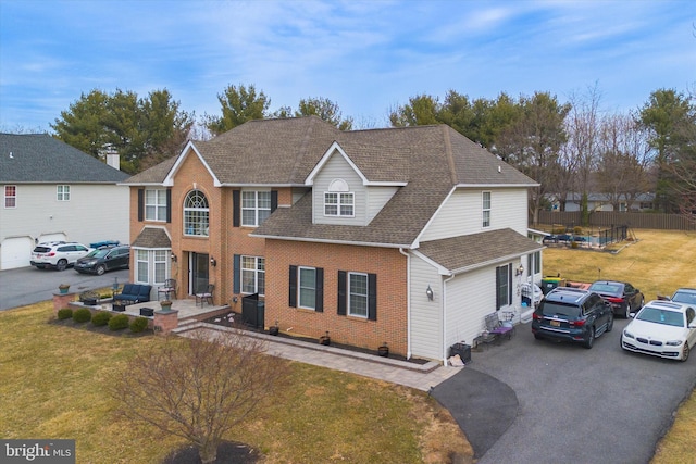 view of front of home featuring driveway, brick siding, roof with shingles, and a front yard